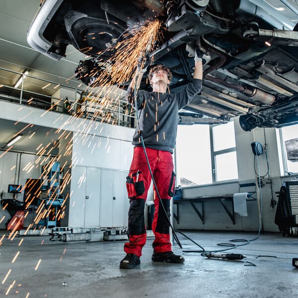 Mechaniker arbeitet bei Auto Bernhard mit der Flex am Unterboden eines Autos auf der Hebebühne