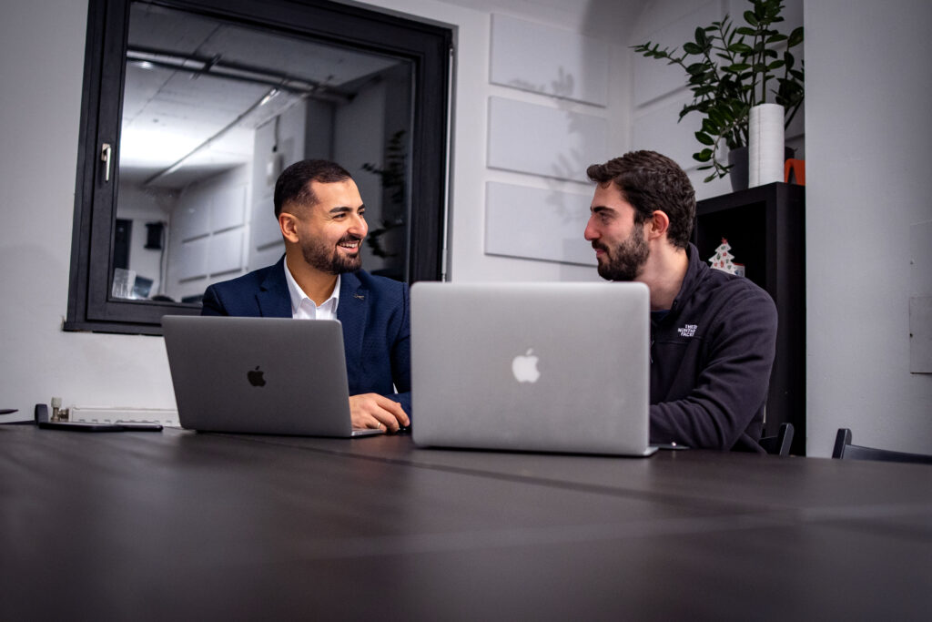 zwei Personen sitzen an einem Tisch mit zwei Laptops und sehen sich an